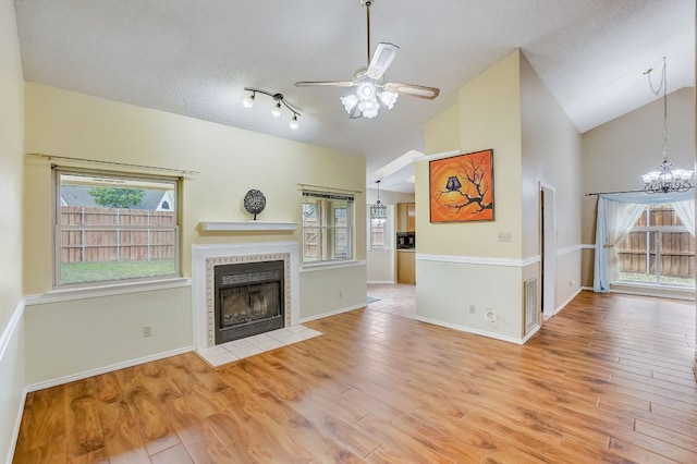 unfurnished living room featuring a textured ceiling, a tile fireplace, ceiling fan with notable chandelier, and light wood-type flooring