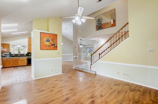 interior space with a skylight, light hardwood / wood-style floors, high vaulted ceiling, and ceiling fan