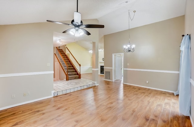 unfurnished living room featuring a fireplace, ceiling fan with notable chandelier, lofted ceiling, and light wood-type flooring