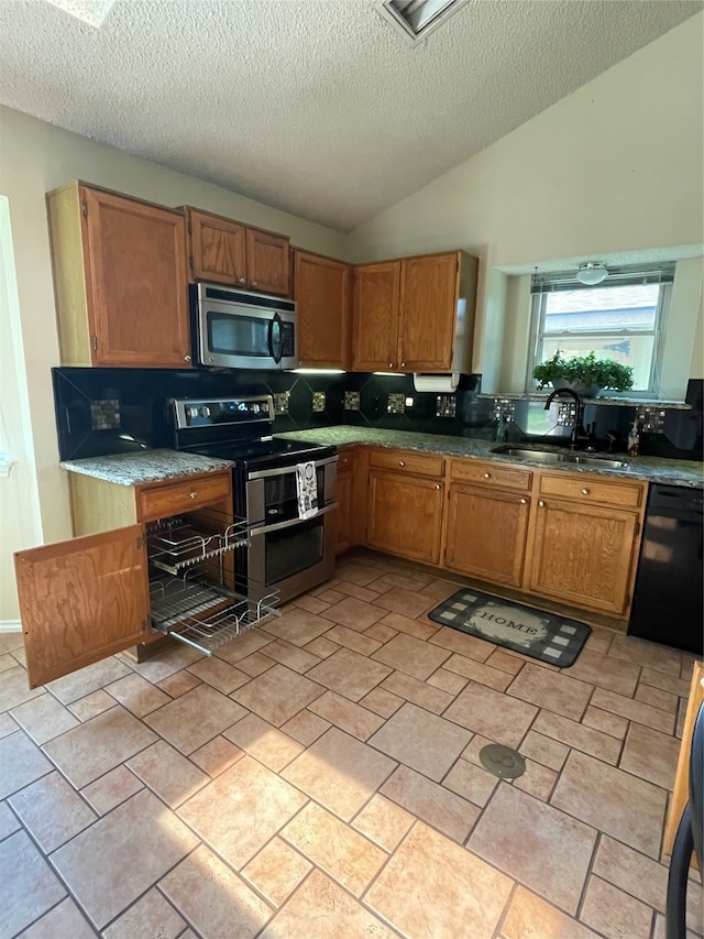 kitchen with lofted ceiling, sink, a textured ceiling, appliances with stainless steel finishes, and tasteful backsplash