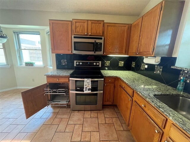 kitchen with decorative backsplash, a textured ceiling, stainless steel appliances, and light stone countertops