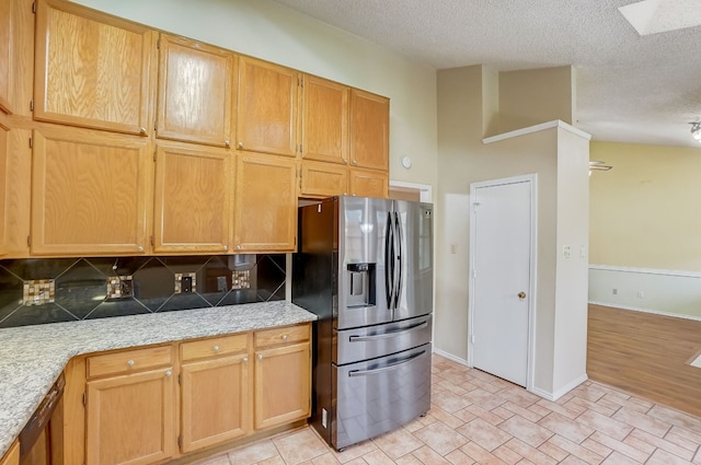 kitchen featuring decorative backsplash, stainless steel fridge, a skylight, a textured ceiling, and high vaulted ceiling