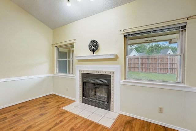 unfurnished living room with a textured ceiling, a tile fireplace, hardwood / wood-style floors, and vaulted ceiling