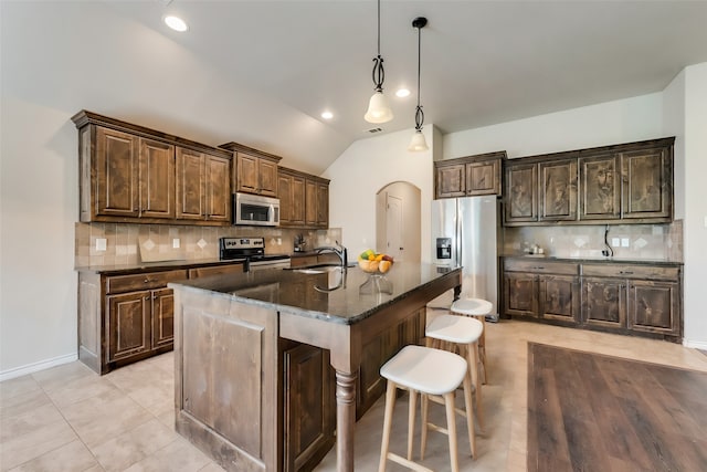 kitchen with a kitchen island with sink, sink, vaulted ceiling, backsplash, and appliances with stainless steel finishes