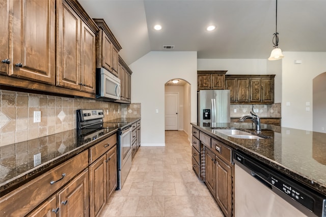 kitchen with sink, lofted ceiling, decorative backsplash, appliances with stainless steel finishes, and dark stone countertops