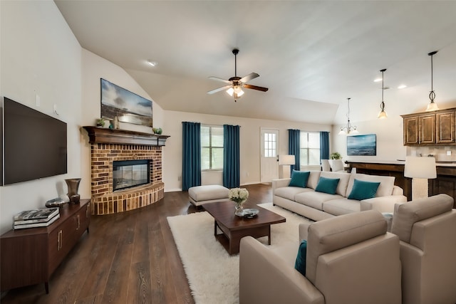 living room featuring ceiling fan with notable chandelier, vaulted ceiling, dark hardwood / wood-style floors, and a fireplace