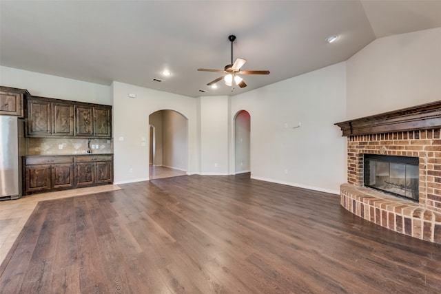 unfurnished living room with a brick fireplace, lofted ceiling, ceiling fan, and wood-type flooring