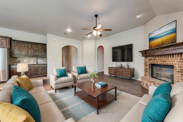 living room featuring a brick fireplace, lofted ceiling, light hardwood / wood-style floors, and ceiling fan