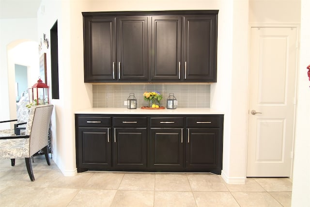 bar with dark brown cabinets, tasteful backsplash, and light tile floors