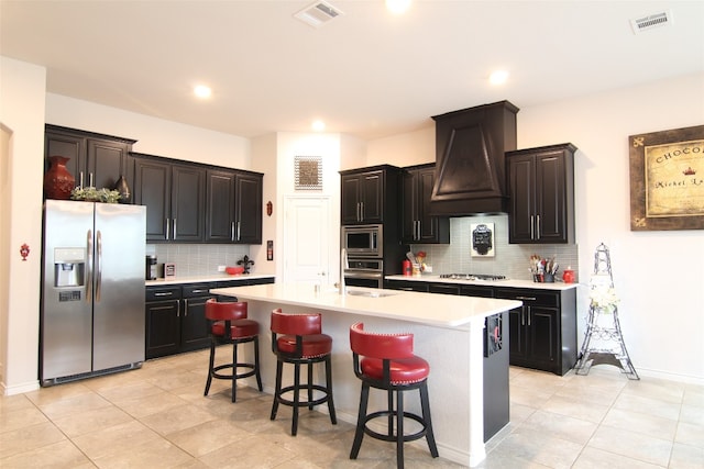 kitchen with a center island with sink, backsplash, custom exhaust hood, and stainless steel appliances