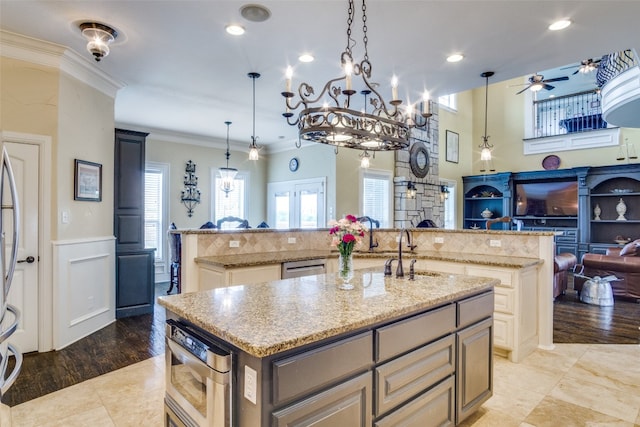 kitchen with backsplash, ceiling fan with notable chandelier, an island with sink, light tile floors, and ornamental molding