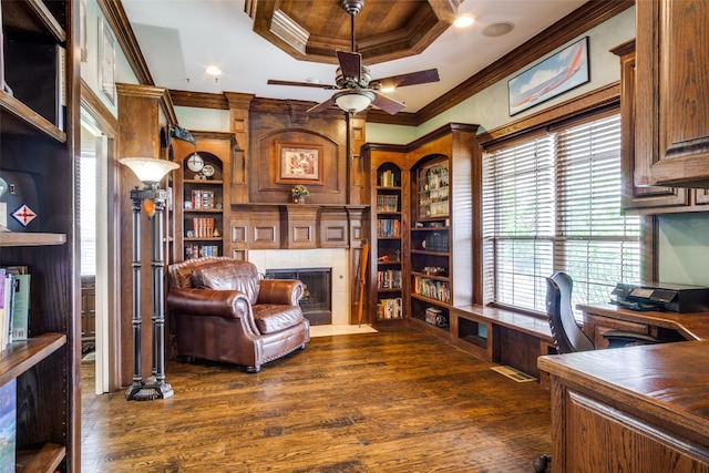 home office featuring ceiling fan, a raised ceiling, a tiled fireplace, dark wood-type flooring, and crown molding