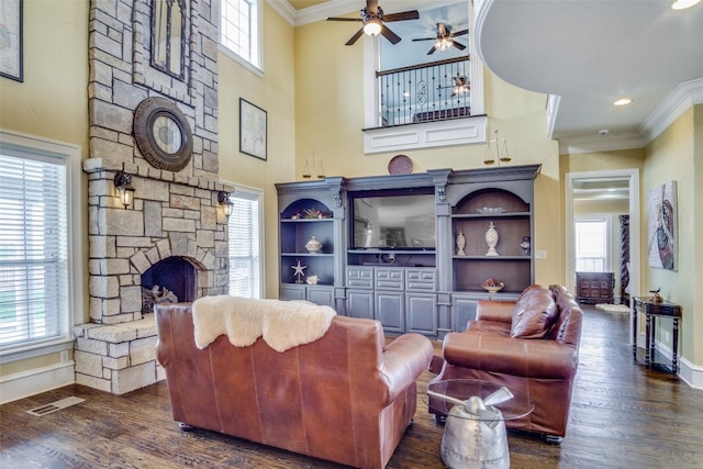 living room with ceiling fan, crown molding, a high ceiling, dark hardwood / wood-style floors, and a fireplace