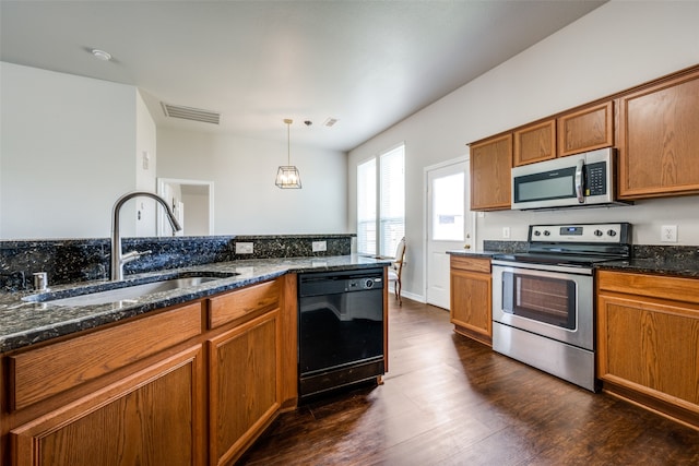 kitchen with dark stone counters, stainless steel appliances, sink, decorative light fixtures, and dark wood-type flooring