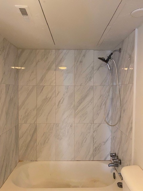 bathroom featuring toilet and tiled shower / bath