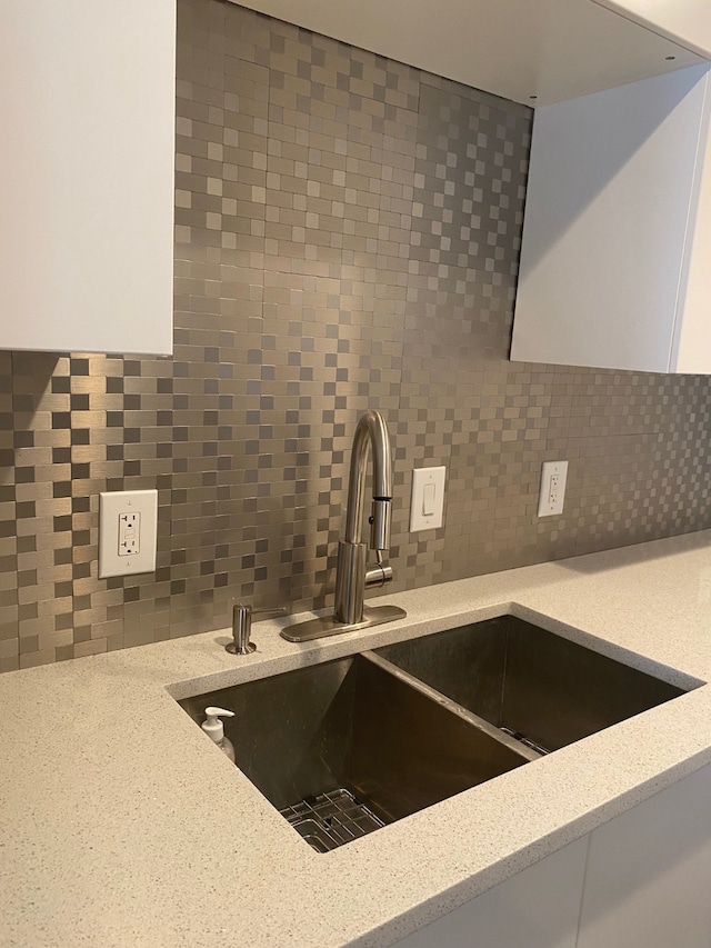 interior details featuring white cabinetry, light stone counters, sink, and tasteful backsplash