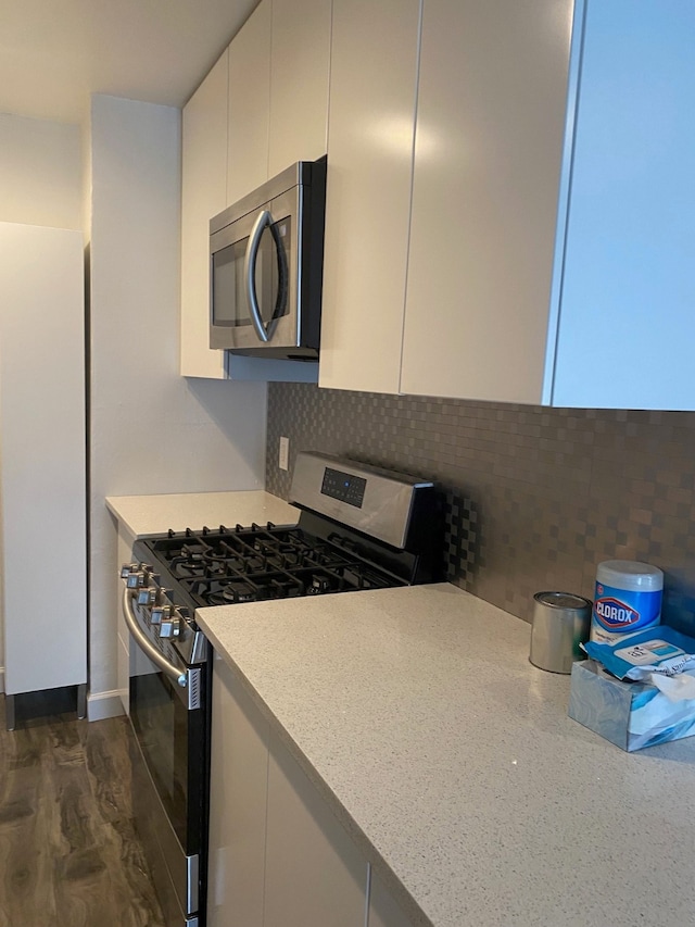 kitchen featuring light stone counters, dark hardwood / wood-style floors, stainless steel appliances, tasteful backsplash, and white cabinetry