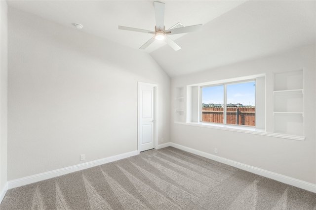 empty room with vaulted ceiling, carpet floors, built in shelves, and ceiling fan