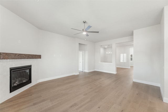 unfurnished living room featuring a tiled fireplace, light wood-type flooring, and ceiling fan with notable chandelier