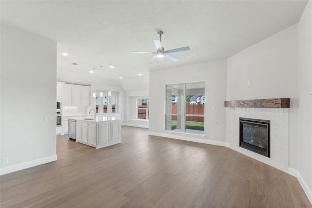 unfurnished living room featuring light hardwood / wood-style floors, sink, a tile fireplace, and ceiling fan