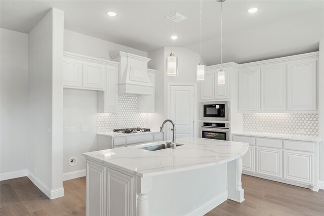 kitchen featuring a center island with sink, sink, light stone countertops, white cabinetry, and appliances with stainless steel finishes