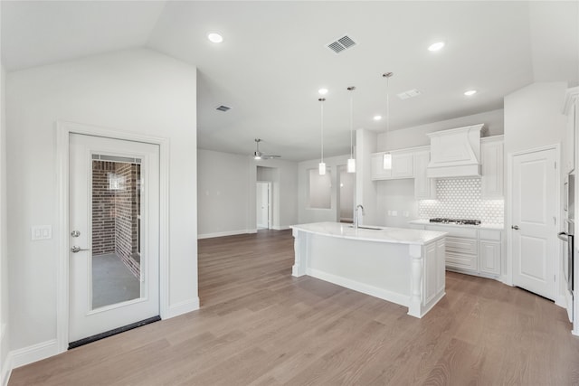 kitchen with a center island with sink, premium range hood, vaulted ceiling, pendant lighting, and light hardwood / wood-style floors