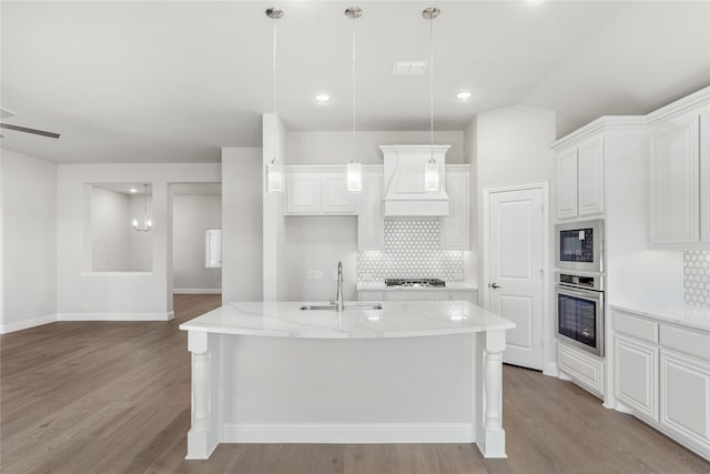 kitchen featuring oven, white cabinets, light stone counters, an island with sink, and sink