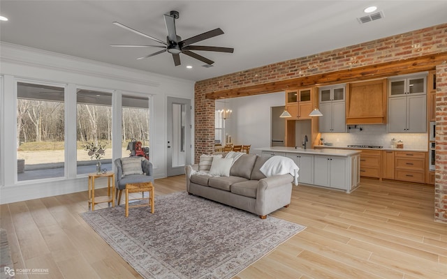 living room featuring ceiling fan with notable chandelier, light hardwood / wood-style flooring, and brick wall