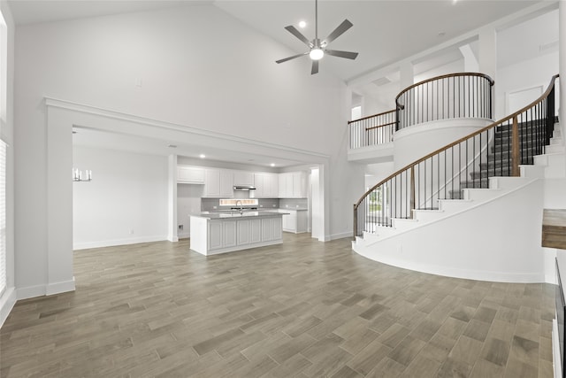 unfurnished living room featuring light hardwood / wood-style floors, ceiling fan, high vaulted ceiling, and sink