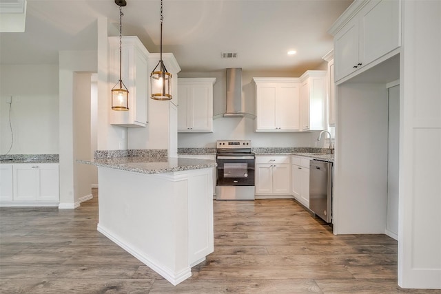 kitchen with wall chimney range hood, stainless steel appliances, white cabinetry, and light hardwood / wood-style floors