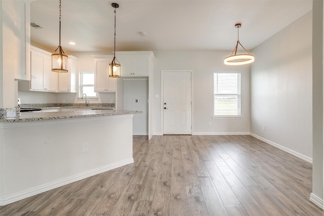 kitchen featuring plenty of natural light, decorative light fixtures, white cabinetry, and light stone counters