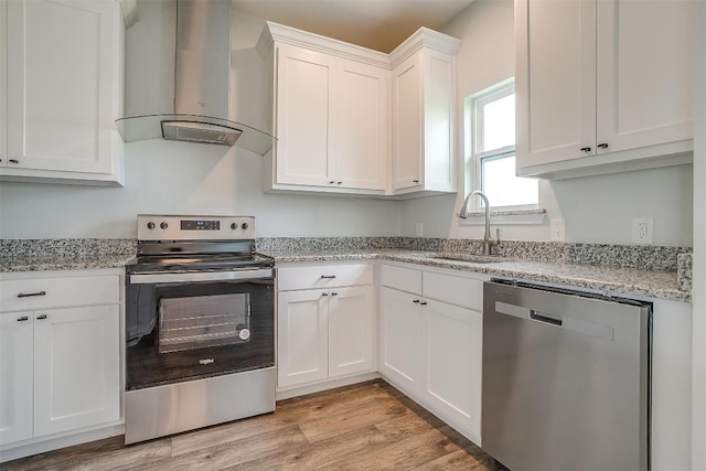 kitchen featuring stainless steel appliances, light hardwood / wood-style floors, wall chimney range hood, white cabinetry, and sink