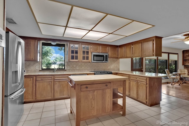 kitchen with light tile patterned floors, appliances with stainless steel finishes, a kitchen island, and ceiling fan