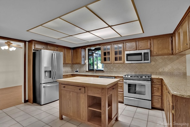 kitchen featuring light tile patterned floors, stainless steel appliances, ceiling fan, decorative backsplash, and wooden counters