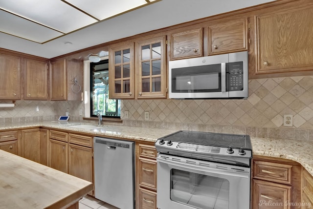 kitchen with backsplash, light tile patterned floors, light stone counters, sink, and appliances with stainless steel finishes