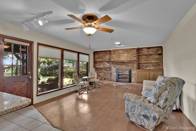 tiled living room with a brick fireplace, brick wall, rail lighting, ceiling fan, and ornamental molding