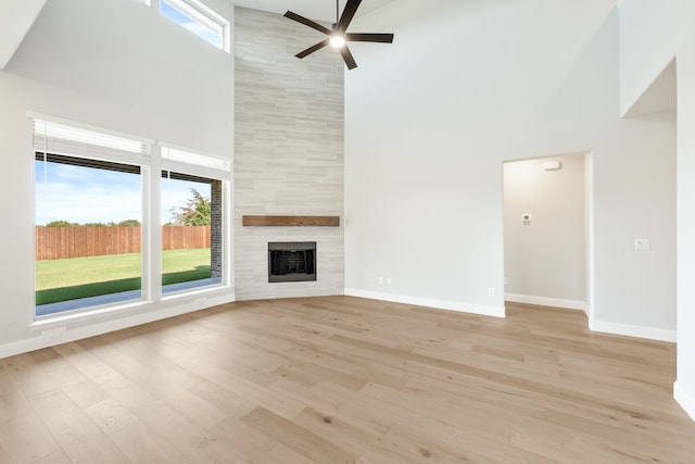 unfurnished living room with ceiling fan, a towering ceiling, light hardwood / wood-style flooring, and a fireplace