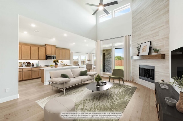 living room featuring a tile fireplace, a high ceiling, light wood-type flooring, and ceiling fan