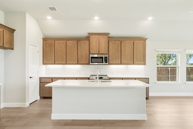 kitchen with light hardwood / wood-style floors, a kitchen island with sink, vaulted ceiling, and backsplash