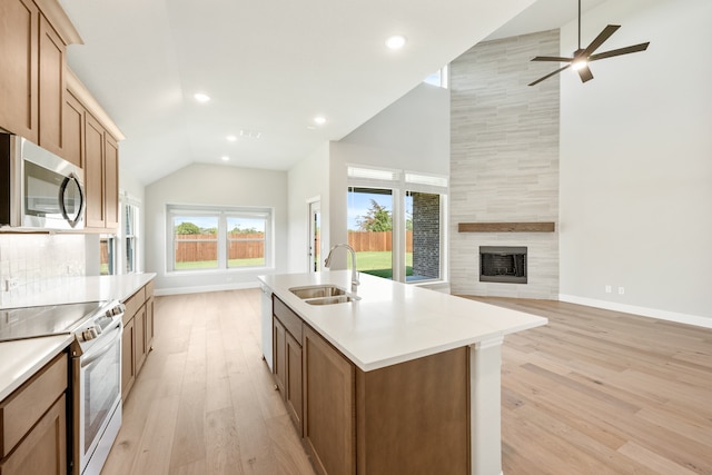 kitchen with a kitchen island with sink, sink, light wood-type flooring, appliances with stainless steel finishes, and a fireplace