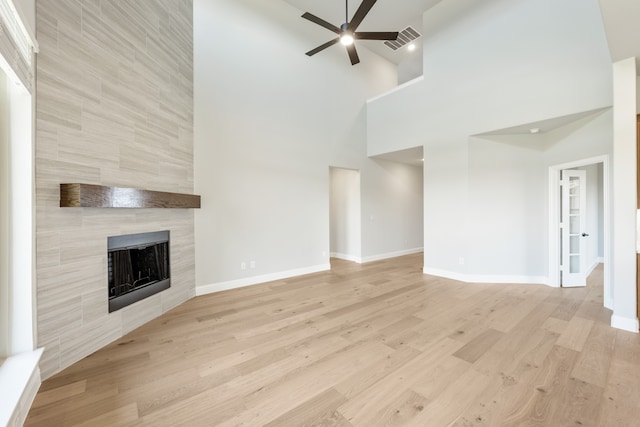 unfurnished living room with ceiling fan, a high ceiling, light wood-type flooring, and a fireplace