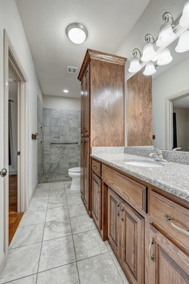 bathroom with vanity, tiled shower, tile patterned floors, toilet, and a textured ceiling