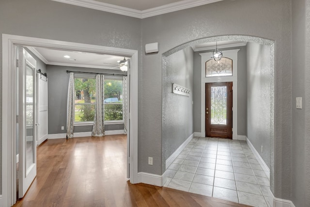 tiled foyer entrance with a barn door, ceiling fan, and crown molding