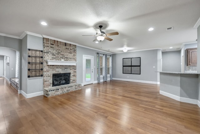 unfurnished living room featuring ceiling fan, crown molding, light hardwood / wood-style flooring, a textured ceiling, and a brick fireplace