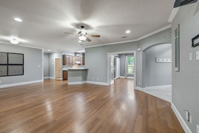 unfurnished living room with a textured ceiling, ornamental molding, hardwood / wood-style floors, and ceiling fan