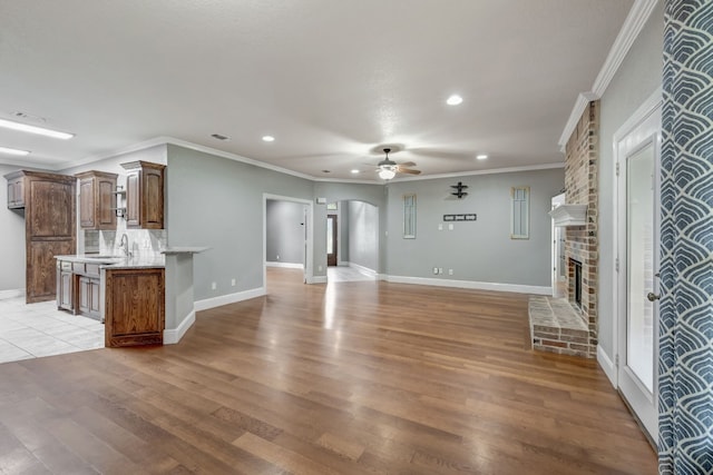 unfurnished living room featuring a brick fireplace, ceiling fan, light wood-type flooring, and crown molding