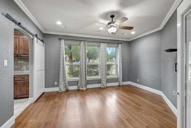 unfurnished dining area with a barn door, light wood-type flooring, a textured ceiling, ceiling fan, and ornamental molding