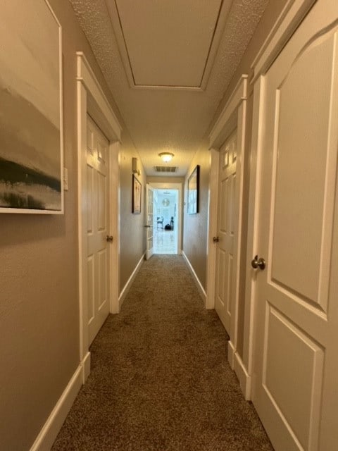 corridor featuring a textured ceiling and dark colored carpet