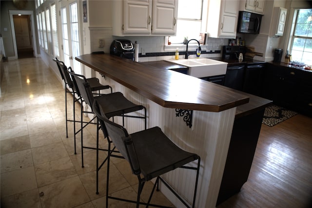 kitchen featuring backsplash, black appliances, white cabinets, a kitchen breakfast bar, and wood counters