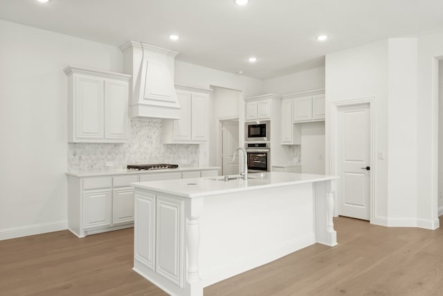 kitchen with hardwood / wood-style floors, a kitchen island with sink, sink, and white cabinets